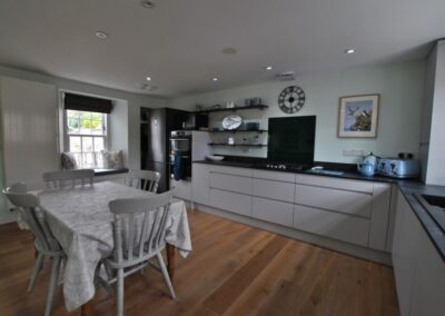 Modern, white and black kitchen units. Wooden floor and table with four chairs.