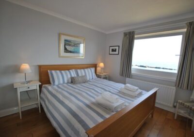 Wooden frame king size bed with white and blue striped linen. The window looks out to the sea.