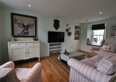Sofa and two armchairs pointing towards a TV. There is a window on the right and a large painting of a deer on the wall to the left of the TV.