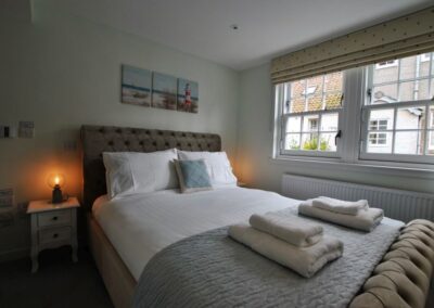 Kingside bed parallel to two sash windows with blinds.