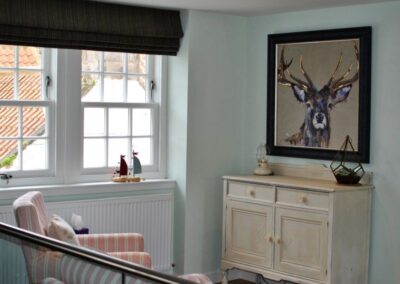 Painting of a stag above a sideboard unit to the right of a window.