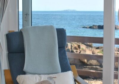 Close-up of blue chair with a blanket and cushion with a sea bird motif in front of a window out to the sea.