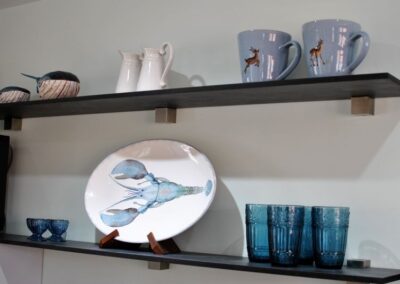 Two shelves with mugs, glasses and plates. The plate has a blue lobster design.