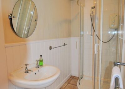 Corner shower unit on tiled floor with white sink beneath round mirror opposite heated towel rail