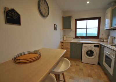 L-shaped kitchen with washing machine and oven beneath counter. Breakfast bar on left.