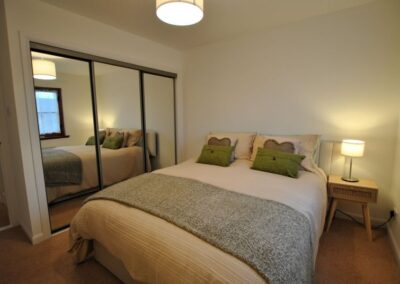 Double bed with bedside table and lamp on the right and built-in mirrored wardrobe on left.