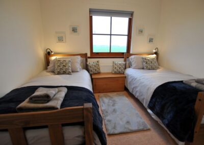 Two single beds with warm blankets either side of a square window.