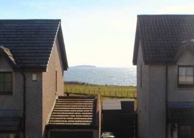 View between two houses towards the Isle of May on a shimmering sea.