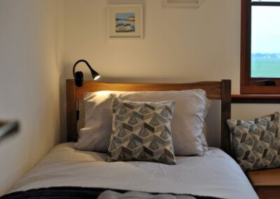 Close-up of single bed pillow with plenty of pillows and an adjustable lamp clamped to the headboard.