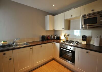 Kitchen with light cupboards and a dark counter top. Oven, gas hob and microwave oven.
