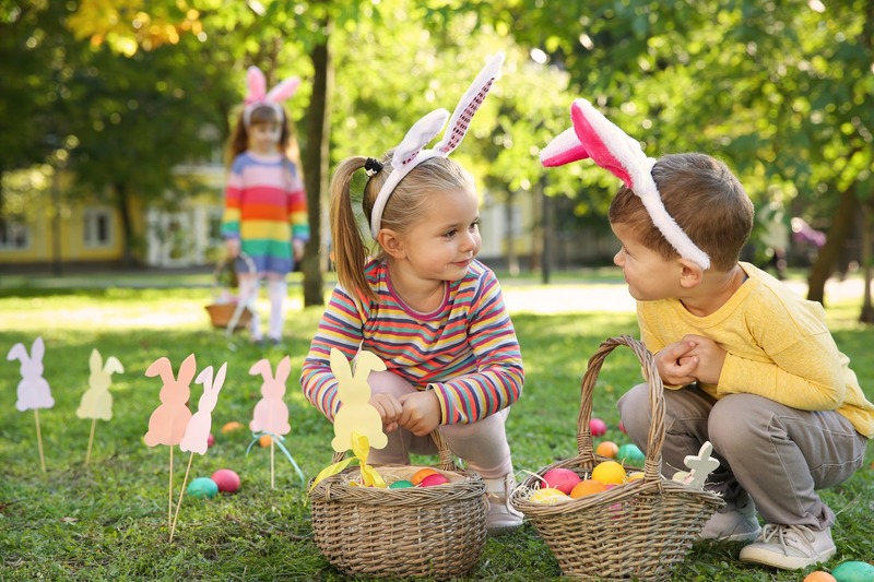 Two children wearing bunny ears crouching over baskets of Easter eggs.