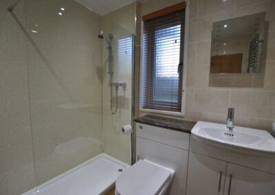 White bathroom suite. Shower and clear shower screen to the left of a narrow window.
