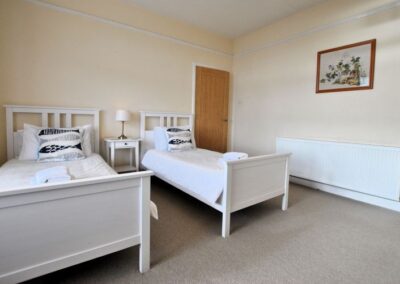 The beds have white wooden bases and white linen. There is a painting on the wall above the radiator.