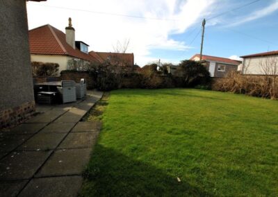 Large grass area in the enclosed garden with patio and seated area next to the house.