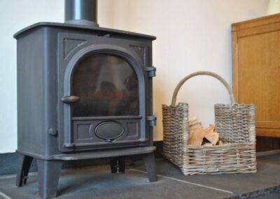 Wood burning stove on stone floor. There is a wicker basket of wood to the right.