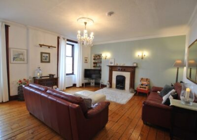 Spackous lounge with two large windows, wooden floor and two leather sofas.