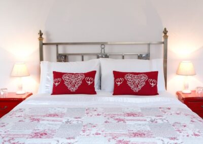 Kingsize bed with metal frame and red and white linen.