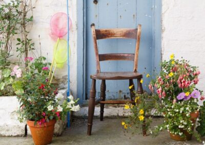 Wooden chair in front of blue wooden door, surrounded by flower pots.