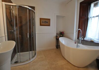 Curved walk-in shower on left with large white stand-alone bath in front of window.