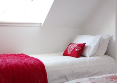 White and red linen on bed beneath window.