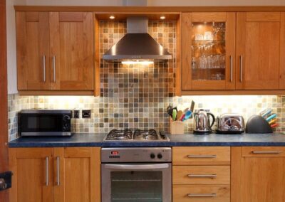 Oven and gas hob with four burners beneath a chrome extractor hood.