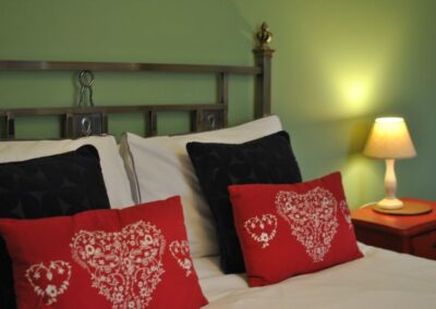 Green walls with red, white and dark cushions and pillows on a white bed.