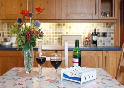 Vase of flowers with two glasses of red wine on kitchen dining table.
