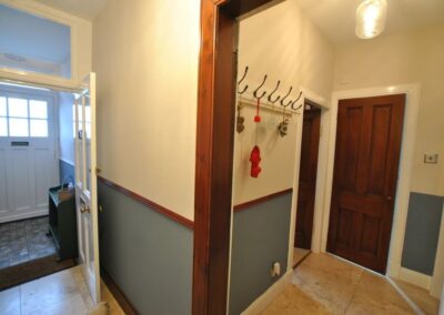 Corner of hallway with front door on the left and five coathooks around the corner on the right.