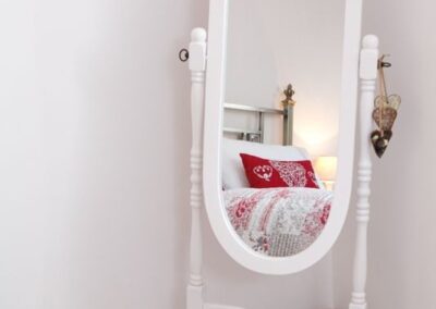 Long, oval mirrir in the corner with reflection of red and white bedding.