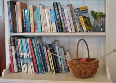 Two shelves of books with basket of wool and knitting needles.