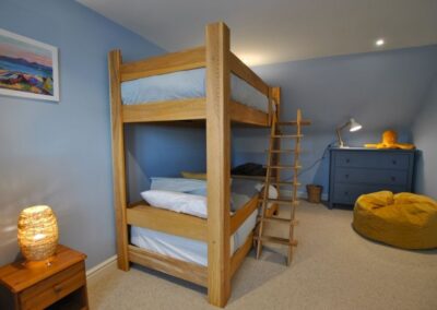 Sturdy wooden bunk bed frame with ladder in a cornflower blue room. There is a blue chest of drawers in the corner behind a mustard-coloured bean bag on the floor.