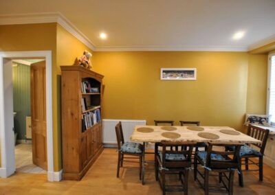 Bright, yellow-orange dining room with bright window on the right and oak bookcase on the left, with a table set for six in between.