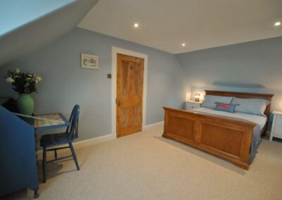 Spacious bedroom with large bed on one side of the door and a writing desk beneath a sloped ceiling on the other.