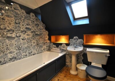 White and dark blue bathroom suite surrounded by Delft blue design tiles. Ther eis a Velux-like window on a sloping ceiling painted a deep blue.
