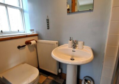 White bathroom suite in a light blue room. There is a window behind he lavatory.