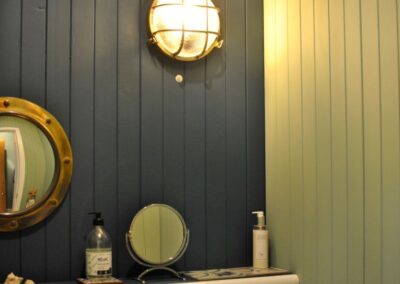 Blue and green wooden walls with nautical lights and porthole-style mirror.