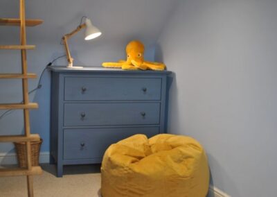 Mustard-yellow bean bag on floor next to similar coloured cuddly octopus on a blue chest of drawers.