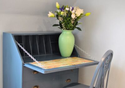 Blue writing desk and chair with lime green vase of fresh flowers.
