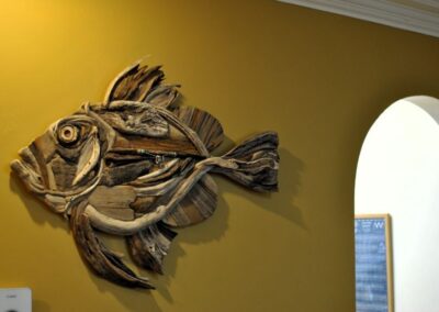 Large wall-mounted sculpture of a fish on a deep yellow wall.
