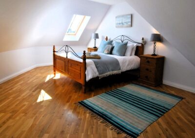 Double bed beneath the eaves on a wooden floor with rug beside bed.