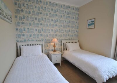 Two single beds with bedside table and lamp between. Blue and white wallpaper behind.