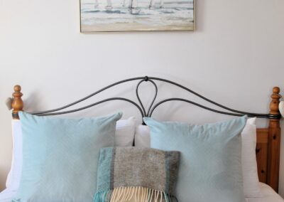 Detail of double bed headboard and pillows with painting on wall behind the bed.