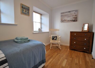 Rocking chair and four-drawer chest of drawers on wooden floor opposite single bed.