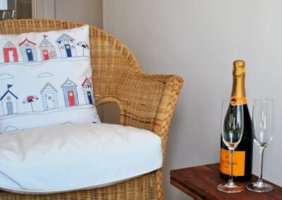 Bottle of fizz with two glasses on small occasional table next to wicker chair.