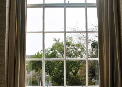 Tall window with long curtains looking out to a tree in the garden.