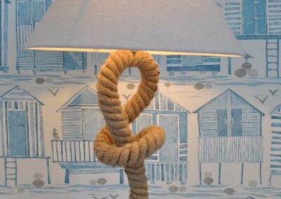 Beside lamp stand looks like a boat rope. Behind is blue and white beach hut design wallpaper.