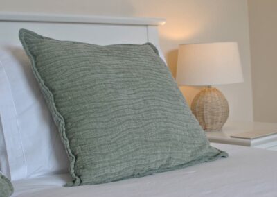 Close-up of mint green cushion on bed with bedside lamp behind.