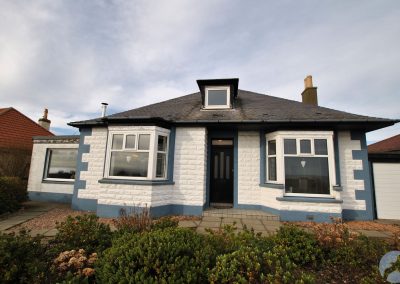 Detatched house with white and blue brickwork, bay windows and small dormer window above front door.
