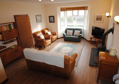 Lounge with aleather sofa and chairs, TV, stove and shelving unit.