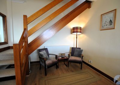 Chairs with coffee table beneath wooden staircase. Behind the chairs are a standard lamp and radiator.